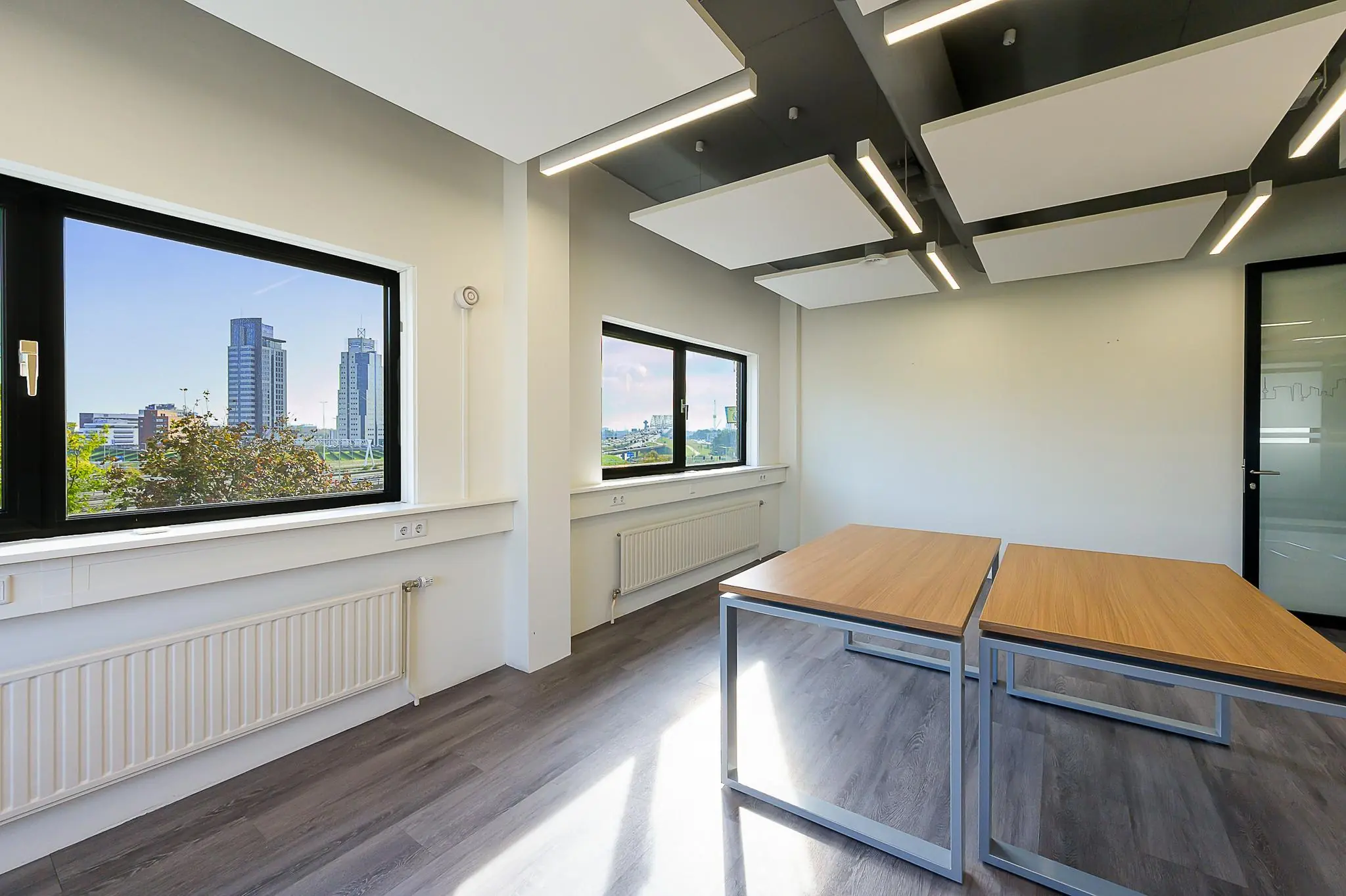 Licht en modern kantoor met houten bureaus aan de K.P. van der Mandelelaan, met uitzicht op Rotterdamse hoogbouw.